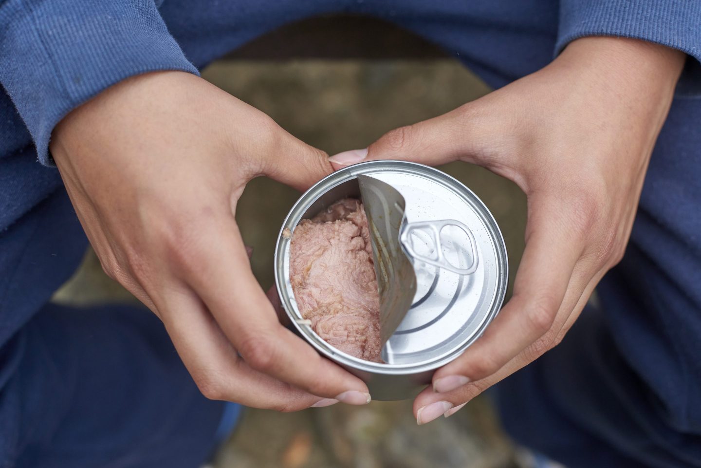 Close-up of a teenage boy's hands opening a can of tuna while camping or hiking in a wilderness area, demonstrating a quick and easy meal option for outdoor adventures